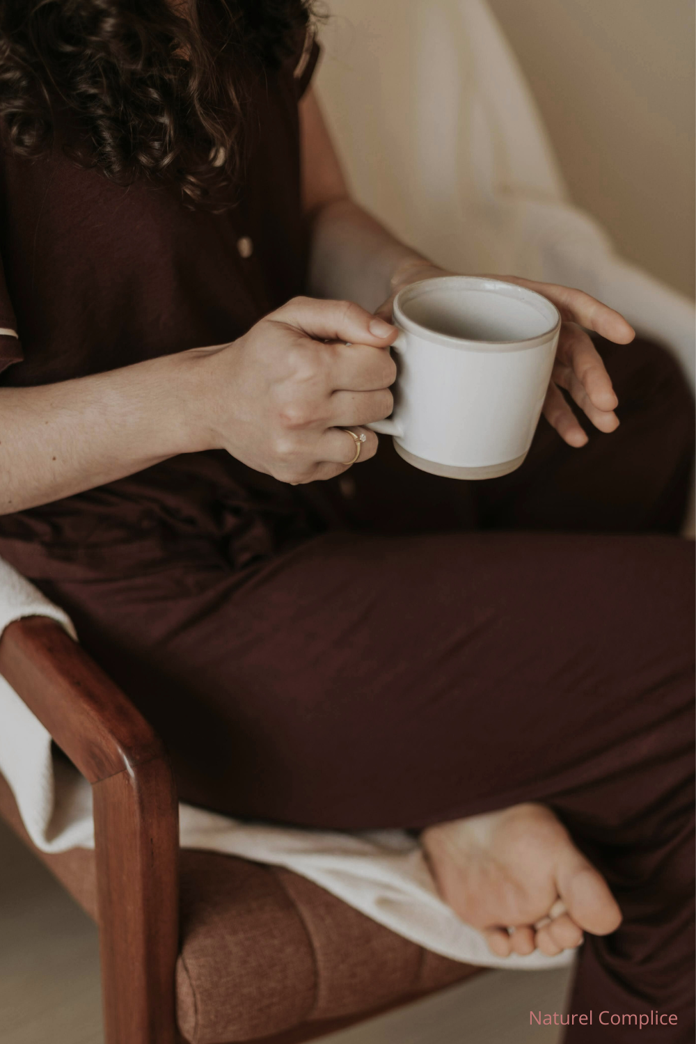 Femme tenant une tasse chaude, assise dans un fauteuil lors d’un moment de pause à la maison