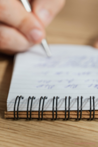 Main écrivant dans un carnet illustrant la prise de recul et la clarification des besoins avant une décision dans le couple