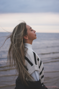 Femme respirant profondément face à la mer, illustration d’une micro-pause physique pour réguler le système nerveux.